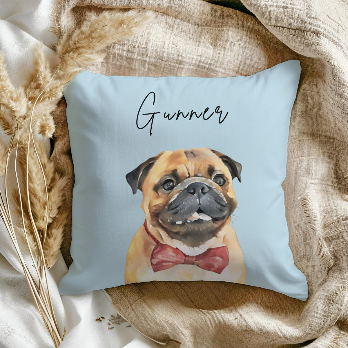 A light blue throw pillow with a watercolor illustration of a pug wearing a red bow tie. The pillow has the name "Gunner" written in black cursive.