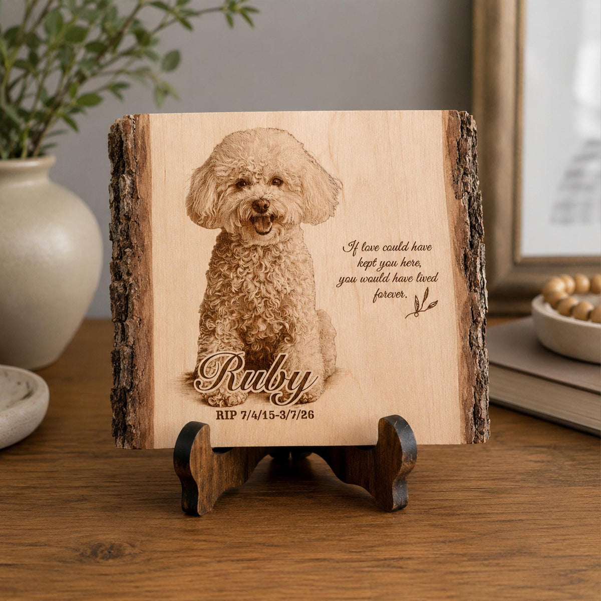 A rectangular wooden plaque with natural bark edges, featuring a laser-engraved portrait of a curly-haired dog. The text reads: Ruby, RIP 7/4/15-3/7/26, and If love could have kept you here, you would have lived forever.