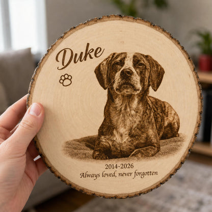 A circular wooden plaque with natural bark edges featuring a laser-engraved portrait of a dog. The text reads Duke, a paw print icon, and the dates 2014-2026 followed by the phrase Always loved, never forgotten.