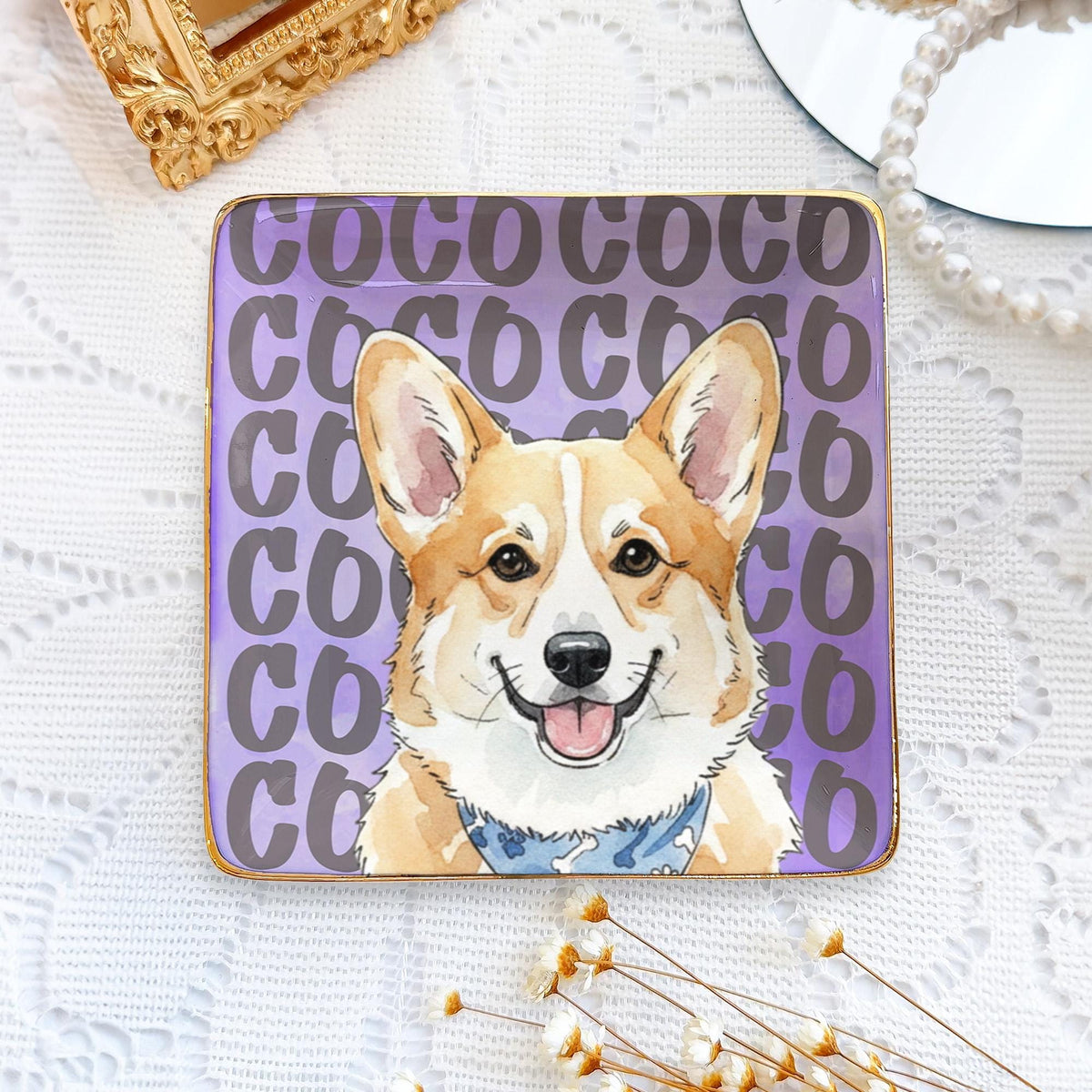 A square ceramic trinket dish with a gold-toned rim featuring a repeating purple text pattern of the word COCO. Centered on the dish is a detailed illustration of a tan and white Corgi dog wearing a blue patterned bandana.