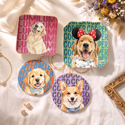 Four ceramic ornaments featuring dog illustrations. One square pink ornament with a golden retriever and text LUMI. One square green ornament with a golden retriever wearing mouse ears and text COOPER. Two round ornaments with a golden retriever and a corgi with text BELLA and COCO.