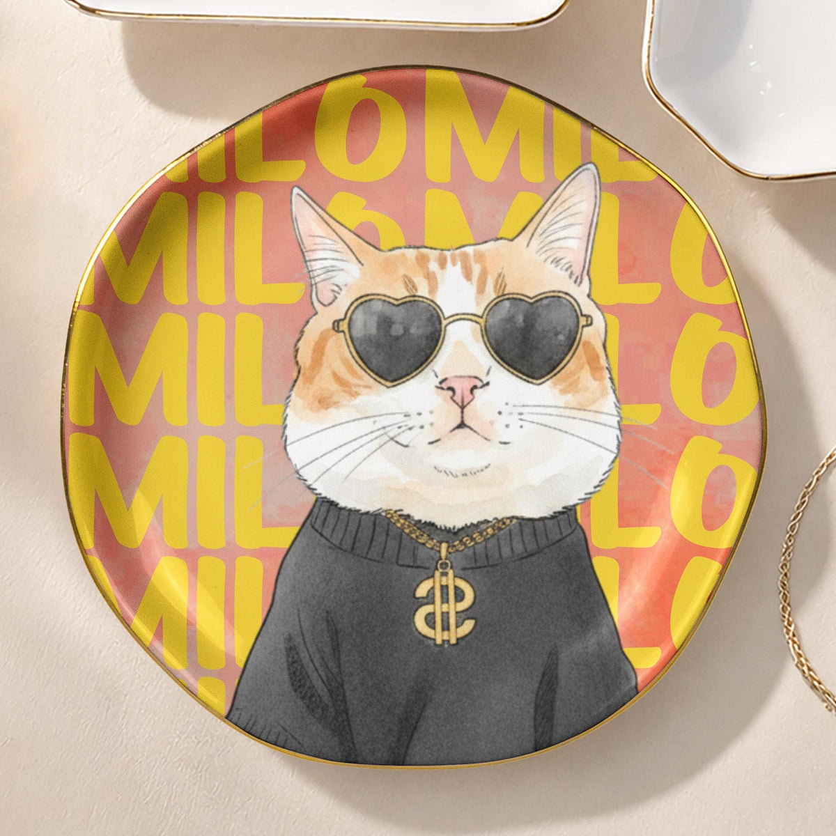 A round ceramic plate with a gold rim featuring a graphic of a ginger and white cat wearing black heart-shaped sunglasses and a gold chain with a dollar sign pendant. The background is a repeating yellow text pattern of the word MILO.
